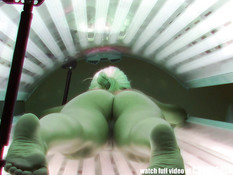 Молодая блондинка с татуировкой на пояснице загорает в солярии