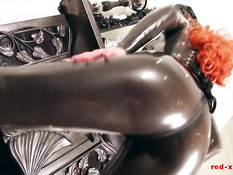 Рыжая шлюха в латексном комбинезоне мастурбирует пизду руками